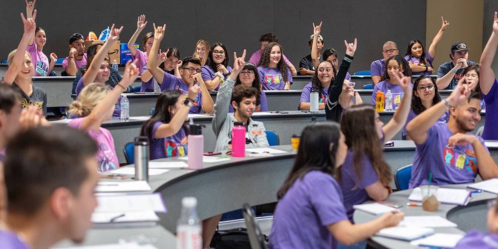 11 students doing the "hook em horns" sign