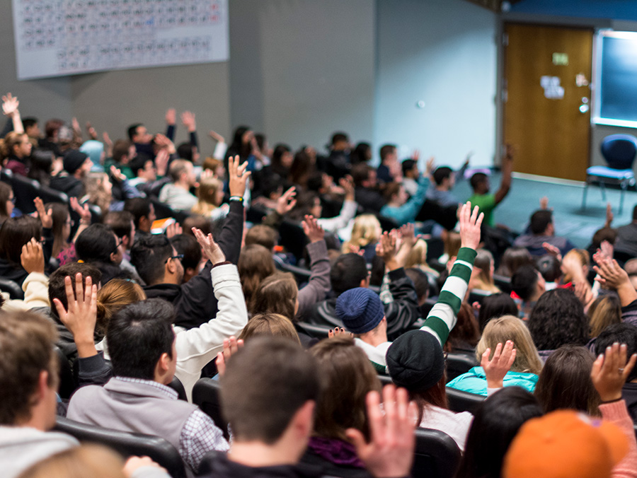 a row of students in a classroom listening to a lecture and taking notes