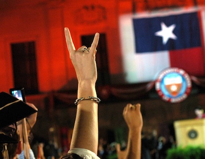 a raised hand shows the hook 'em sign with a Texas state flag in the background